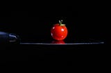 A red tomato balanced on the blade of a sharp knife