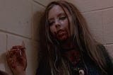 A scary young woman from a horror movie with blood on her face, shirt, and hand.