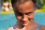 Close up photo of a girl in front of a swimming pool with a devious look on her face.