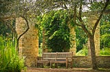 A photo of a bench betweens stone columns of green outdoor foliage