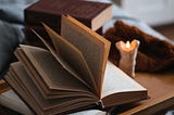 An open book on a little nightstand with a little lit candle next to it.