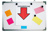 A whiteboard with orange, yellow, pink, and blue sticky notes on it and a paper with a red arrow that reads suggestions.