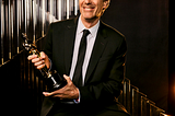 Walter Salles, de terno e gravata, sorridente, posa segurando ao estatueta dourada do Oscar que conquistou na categoria de Melhor Filme Internacional por “Ainda Estou Aqui”
