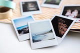 A selection of polaroid photographs sit on a table. The images include beach scenes and people.