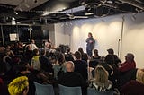 comedian in front of a full crowd in the art space of New Haven
