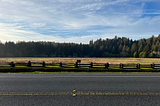 A two-lane road next to an open pasture under blue skys.