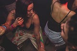 Two young girls dancing close together. They are wearing tank tops and look sweaty.