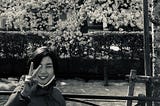 Pre-teen Japanese girl giving the peace sign in front of cherry blossoms.
