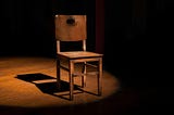A wooden chair spotlighted with a soft light in a dark room.