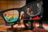 Large pair of black glasses focusing on a stage production with a woman in green, a man in devil horns nad a woman in black.