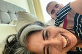 Selfie of Ana Del Castillo and Ken Blackman laughing in bed.