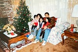Family of 5 sitting at a couch by a Christmas tree