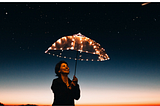 A jubilant woman with brown hair holding a light up umbrella against a twilight background.