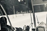 the front of a bus, with a view of the driver and a sign in white cursive lettering that says, “Tiene Memoria la Piel”