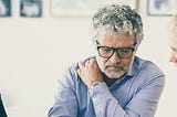 Middle aged father sitting at a table with his two twenty-something daughters. The father is listening to his daughters.