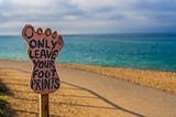 A notice board in the shape of a foot, by the sea, which reads ‘Only leave your foot prints’