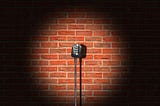 A microphone stand on a stage in a spotlight against a brick wall.
