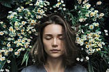 Woman lies with eyes closed in a field of daisies
