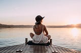 A girl sitting on a deck on water watching the sunset.