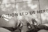 Photo of two sets of feet standing on a pavement with the text “Passion led us here”.