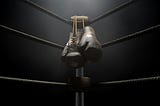 A pair of leather boxing gloves hang off a turnbuckle of a boxing ring