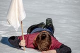 A person lying face down in the snow holding a white flag of surrender.