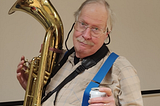 Image of the author with his baritone horn in one hand, a beer in the other, and one of his suspender straps hooked under the thumb of the beer hand.
