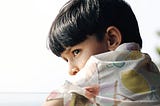 A little boy  dark hair, gazing out of a window with a thoughtful or curious expression.