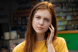 Red-haired woman in yellow shirt looking confused