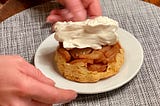A woman serves a portion of Swedish apple pie topped with whipped cream