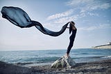 an image of a lady standing on a rock by the sea looking free and tranquil.