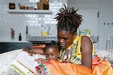 A Black woman reads a book to her child.