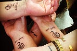 Five white people’s wrists, displaying tattoos