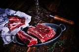 Uncooked high-quality steak fillets on a metal platter, being prepared with salt