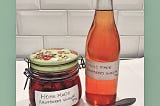 A floral jar containing raspberries and vinegar and a bottle of Raspberry Vinegar Tonic, both are home made by author