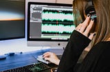 Woman listening to sound played back on sound editing software. She is in a black shirt and has black nail polish and has her hands on the keyboard.