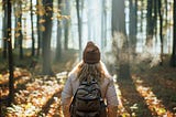 Foggy cold morning weather in autumn. Woman with backpack and knit hat hiking in forest at fall season