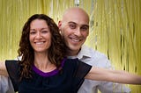 A woman and man smile in front of yellow streamers