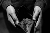 A monochromatic image of a person’s hands holding an empty wallet.