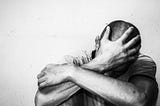 Black and white photo of a man in deep grief, his arms crossed with a hand covering his face.