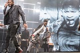 Usher dances on stage in all black in front of background dancers.