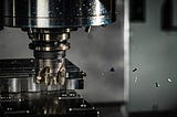 A milling tool is cutting into a piece of metal. The tool is rapidly spinning and chips of metal are flying off of the tool.