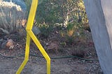 A yellow stick figure holding up a wall leaning into it made of metal artist unknown gallery in Walnut Creek CA 2017