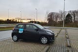 Photo of a Peugeot 108 parked in a parking lot next to a motorway. It has a sticker on it that says Juuve, the name of the rental company.