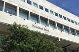 Picture of the exterior of The Juilliard School, with white stone exterior and a blue sky in the background