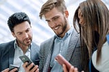 Two guys and a lady smiling while using their phones.