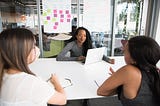 Three women in an office meeting room having a conversation