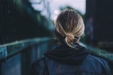 Photo of a person in a leather jacket crossing a bridge taken from behind