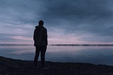 Silhouette of a man standing by a lake in the dark