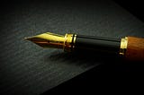 A gold-tipped fountain pen with wood body resting on black notebook